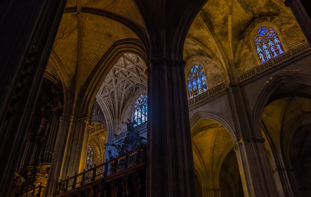 Intérieur d'une cathédrale avec des arches gothiques et des vitraux illuminés.