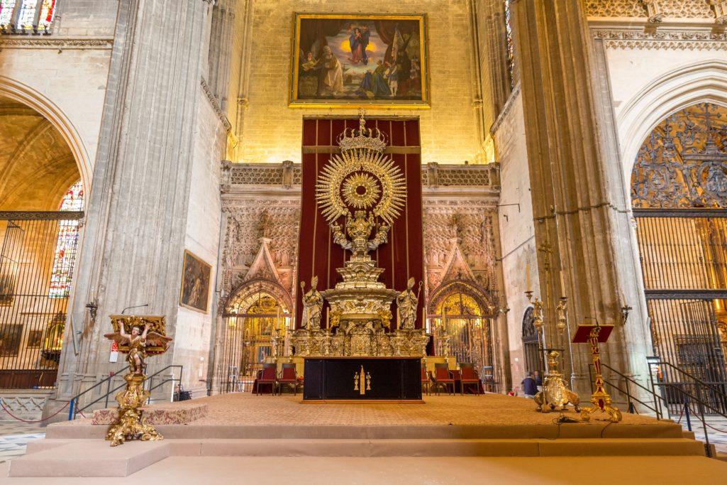 Autel majestueux décoré de dorures, devant un fond de fresques et de tapisseries rouges.