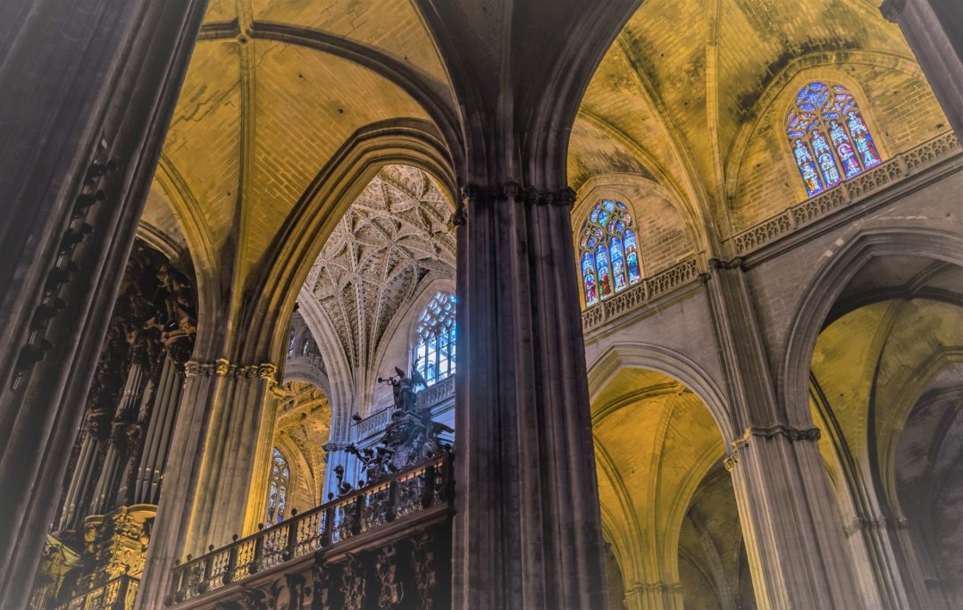 Vue intérieure d'une cathédrale avec des arches et des vitraux colorés.