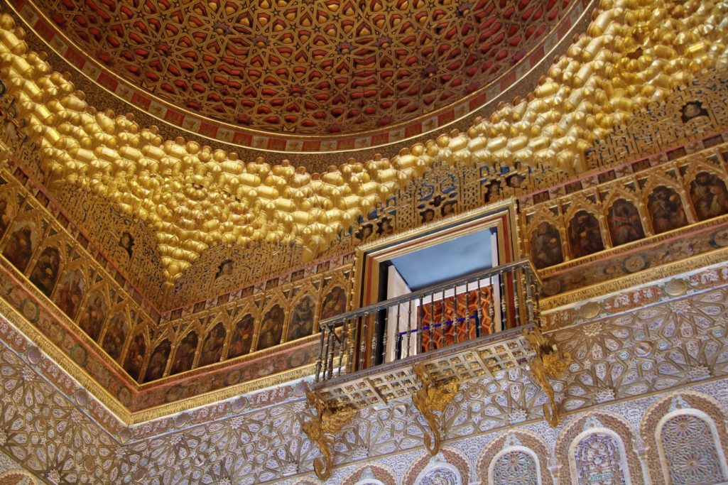 Plafond orné avec motifs géométriques et balcon dans une salle historique.