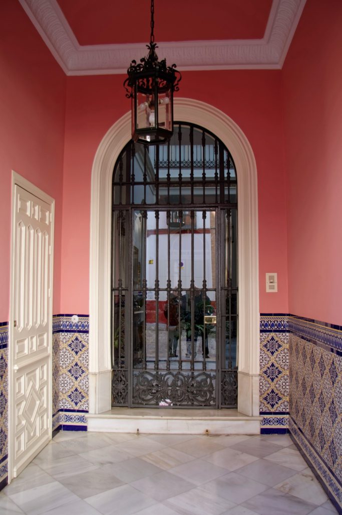 Entrée avec une porte métallique, murs roses et carrelage décoratif.