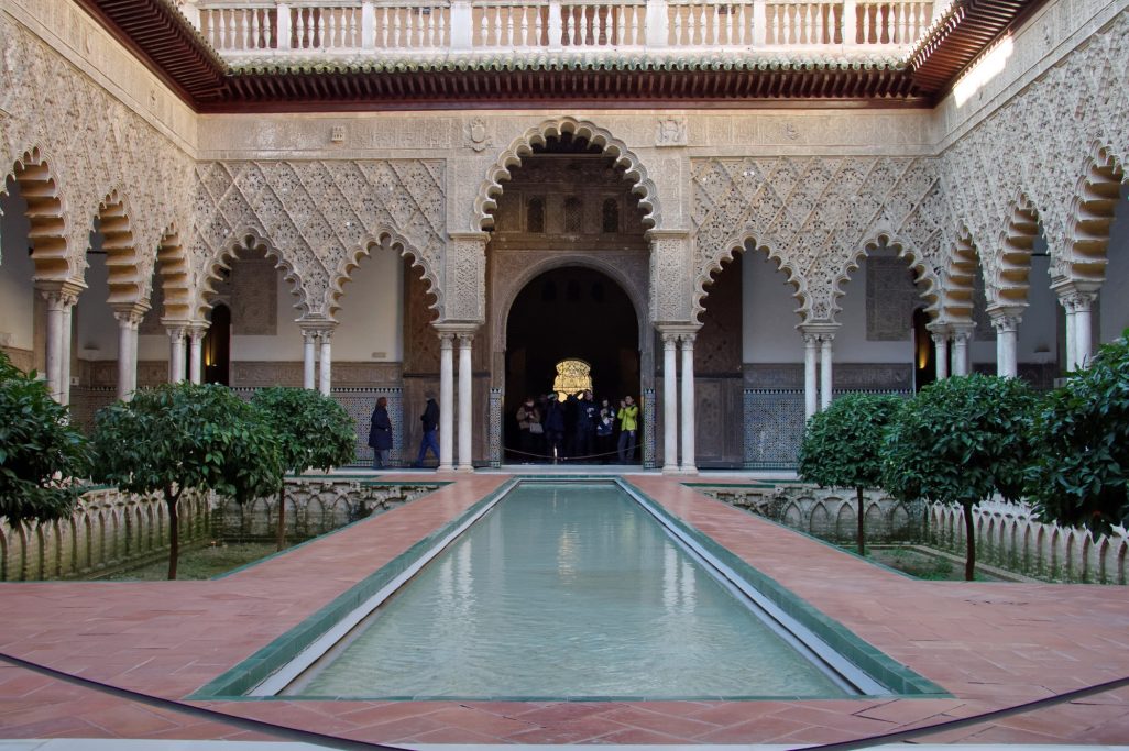 Cour intérieure avec piscine, plantes vertes et arches décoratives mauresques.