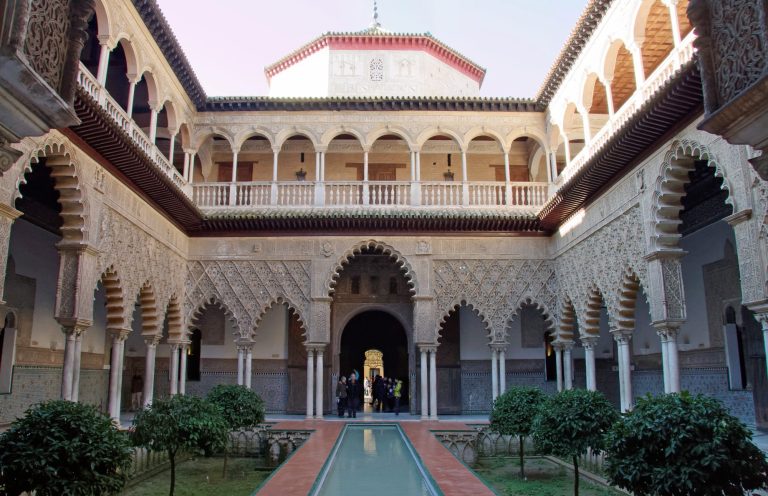 Cour intérieure d'un palais avec arches, colonnes et jardin central verdoyant.
